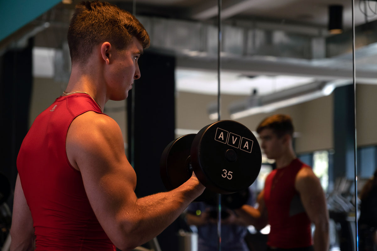 Coach is exercising with weights in a dark gym, focused.